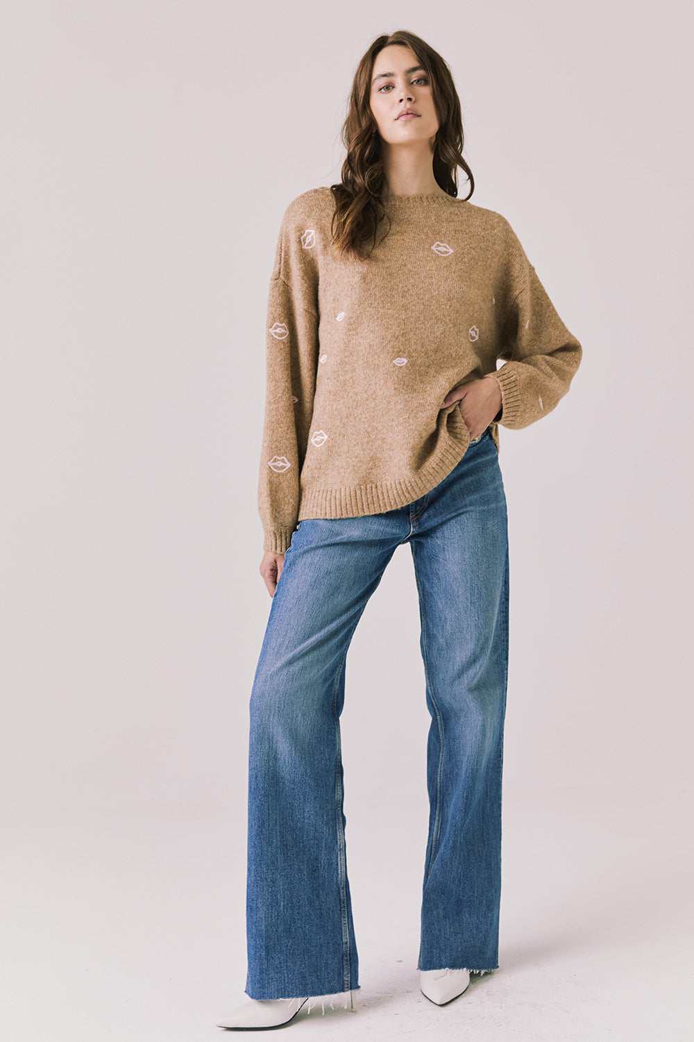 Full body view of woman wearing Chaser’s Love Me Long Sleeve Beige Sweater and blue jeans on a plain background