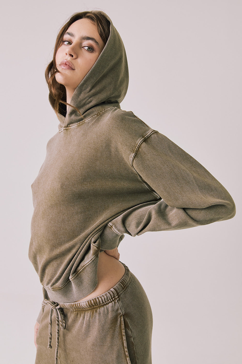 Side view of woman wearing Chaser’s Ginger Brown Martini Pullover Hoodie with hood up on a light pink background