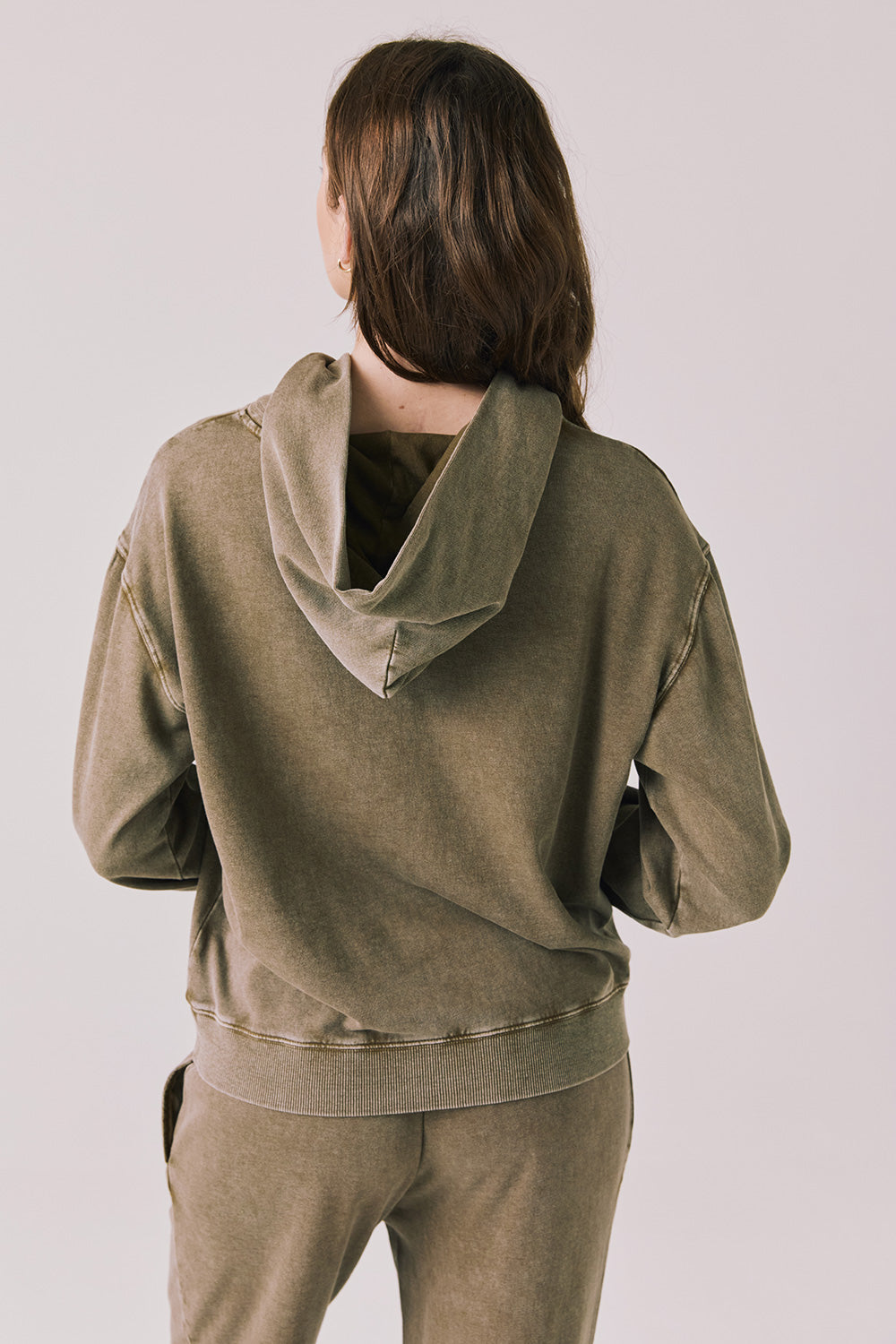 Back view of woman wearing Chaser’s Ginger Brown Martini Pullover Hoodie on a light pink background