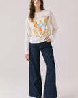 Full body view of woman wearing Chaser’s starry white Willie Nelson Luck Texas Long Sleeve with graphic design and dark blue jeans on a light background (licensed band collaboration)