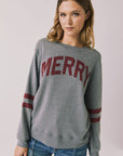 Front view of woman wearing Chaser’s Streaky Grey Merry Long Sleeve with “MERRY” printed in red and red stripes on the sleeves against a plain background