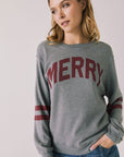 Front view of woman wearing Chaser’s Streaky Grey Merry Long Sleeve with “MERRY” printed in red and red stripes on the sleeves against a plain background