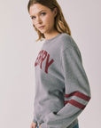  Side view of woman wearing Chaser’s Streaky Grey Merry Long Sleeve with “MERRY” printed in red and red sleeve stripes against a plain background