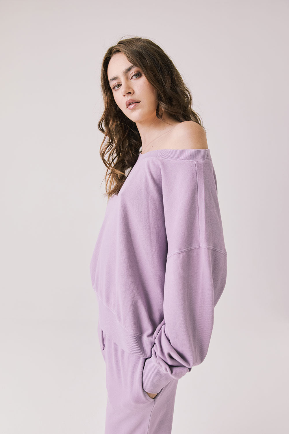 Side view of woman wearing Chaser's Bellini Amethyst Purple Pullover with matching pants on a plain background