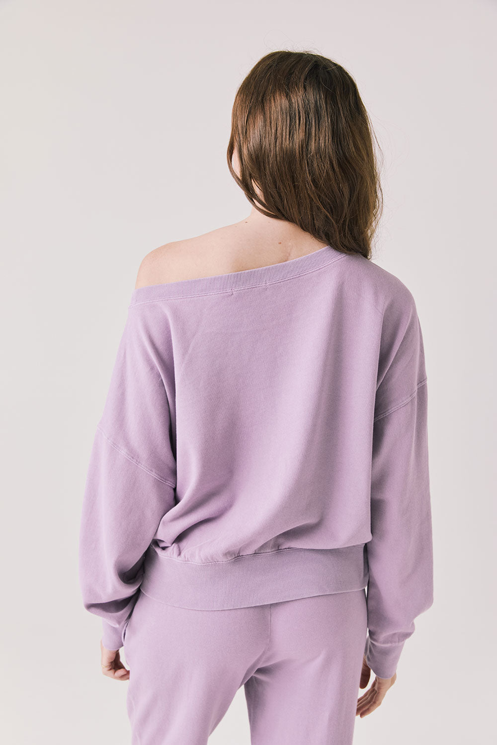 Back view of woman wearing Chaser's Bellini Amethyst Purple Pullover with matching pants on a plain background