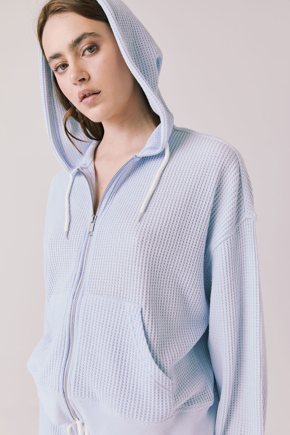 Side view of woman wearing the Abilene Light Skyway Blue Zip Up Hoodie with the hoodie up on a white background