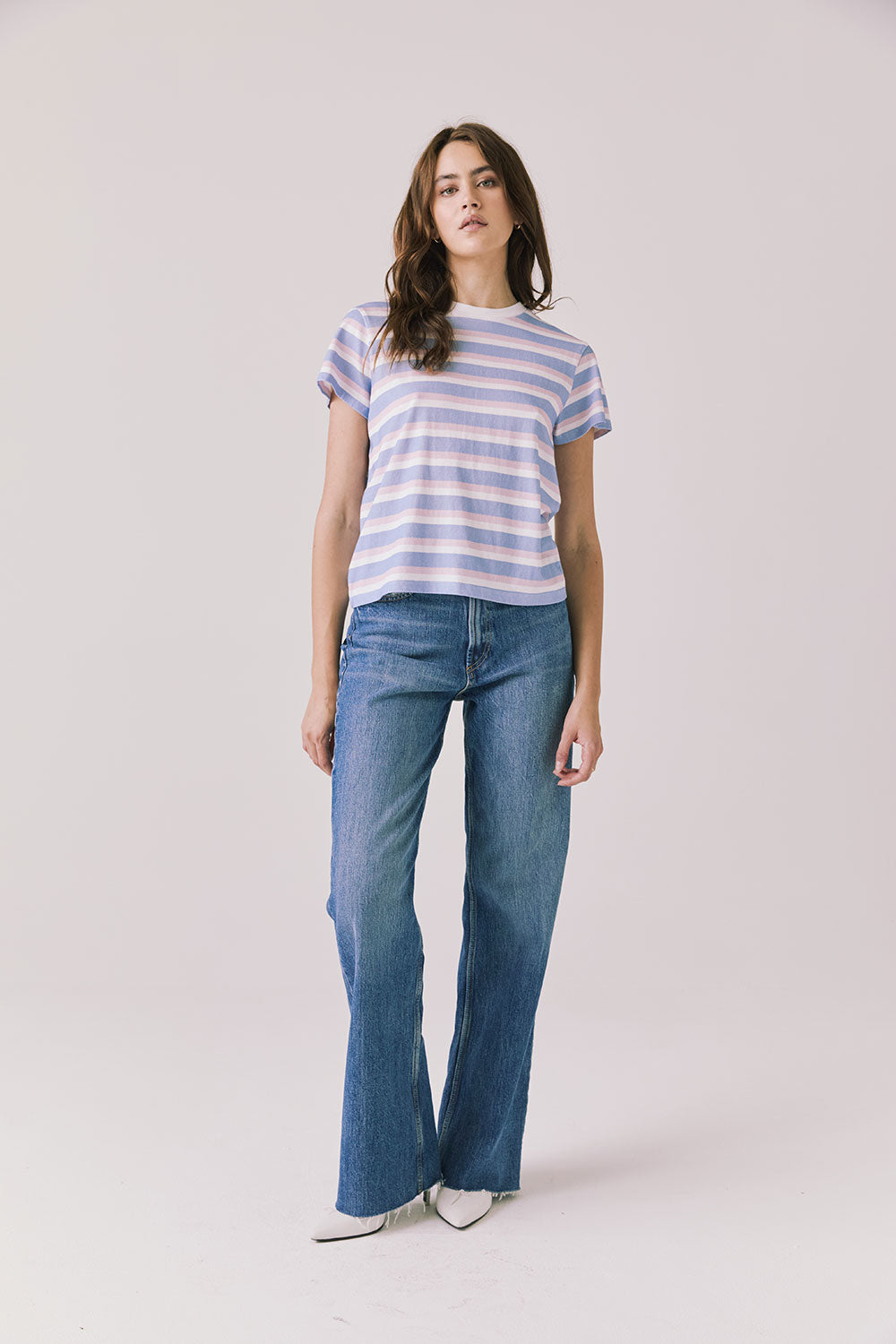 Full body view of woman wearing Chaser’s Cosmo Pink Stripes Tee paired with blue jeans on a white background