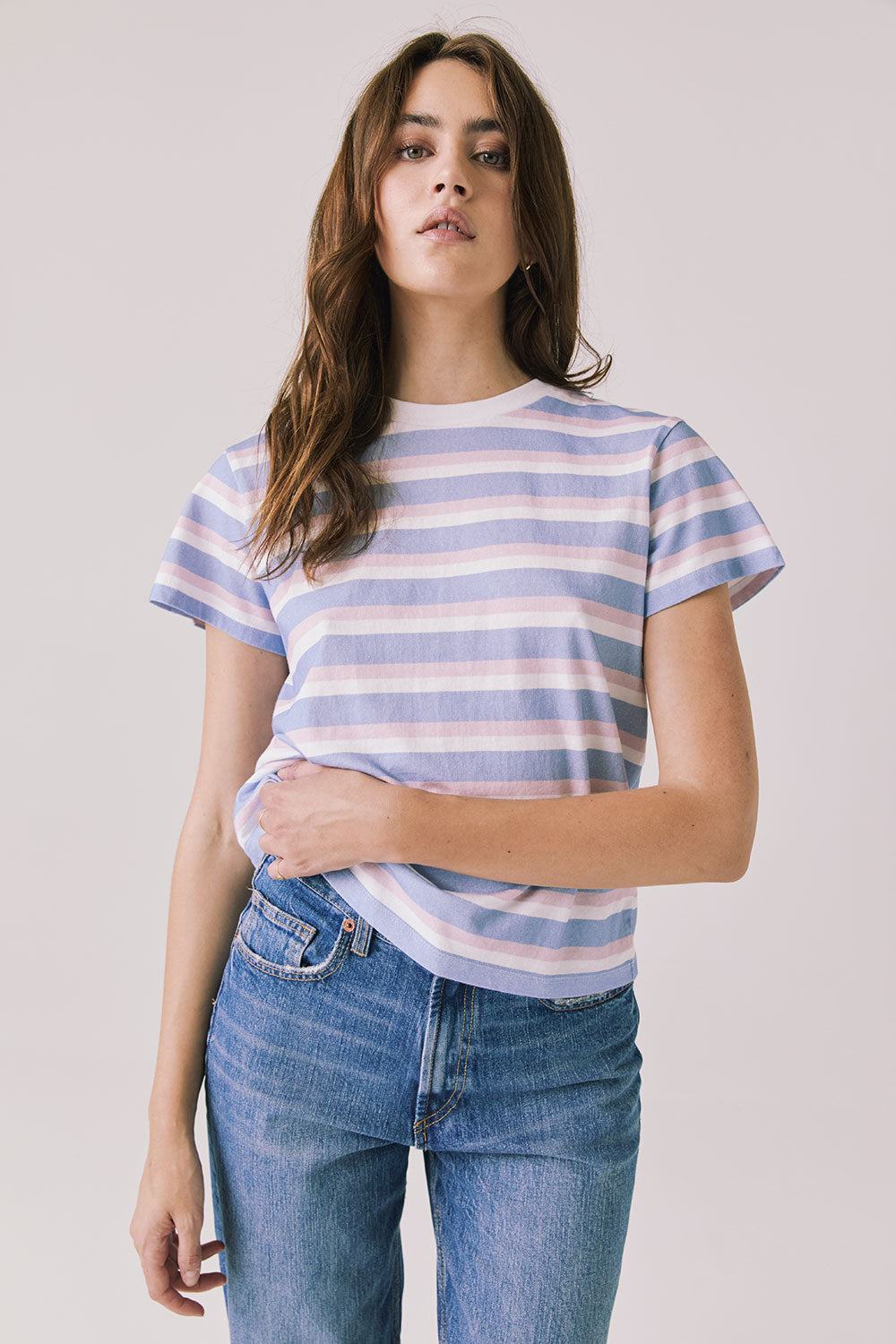 Full body view of woman wearing Chaser’s Cosmo Pink Stripes Tee paired with blue jeans on a white background