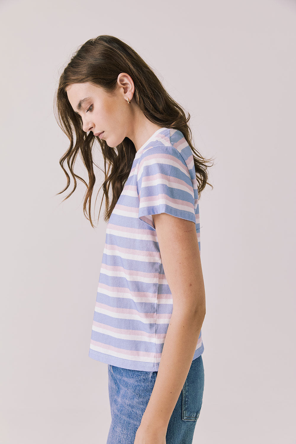 Side view of woman wearing Chaser’s Cosmo Pink Stripes Tee with pink stripe pattern and blue jeans on a white background