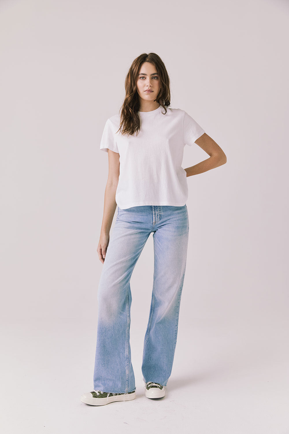 Full body view of woman wearing Chaser’s Cosmo White Tee paired with light blue jeans on a plain background