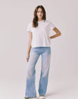Full body view of woman wearing Chaser’s Cosmo White Tee paired with light blue jeans on a plain background