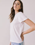 Side view of woman wearing Chaser’s Cosmo White Tee with classic crew neckline and light blue jeans on a plain background
