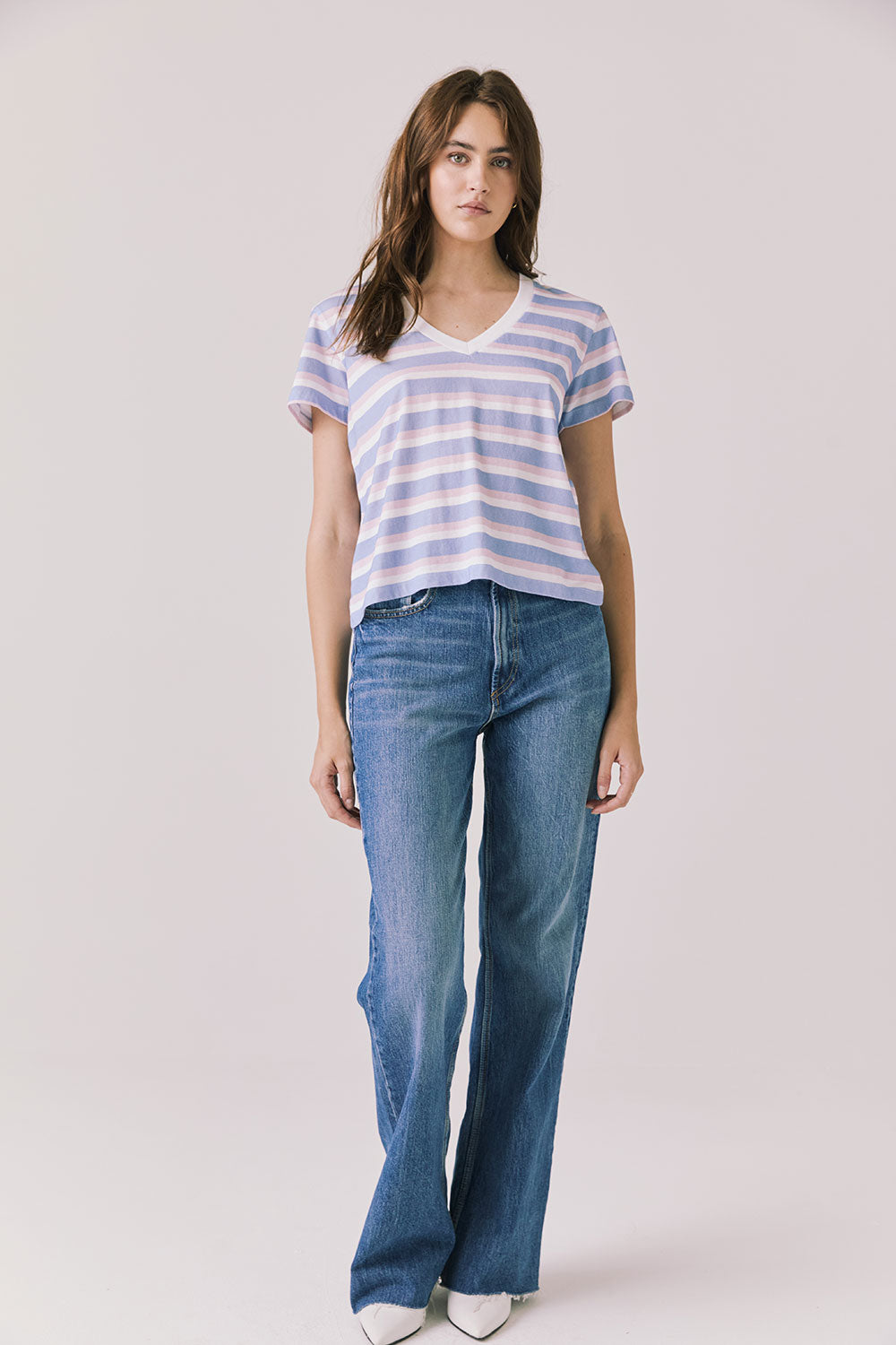 Full body view of woman wearing Chaser’s Gimlet Pastel Stripe Tee with blue jeans on a plain background