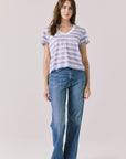 Full body view of woman wearing Chaser’s Gimlet Pastel Stripe Tee with blue jeans on a plain background