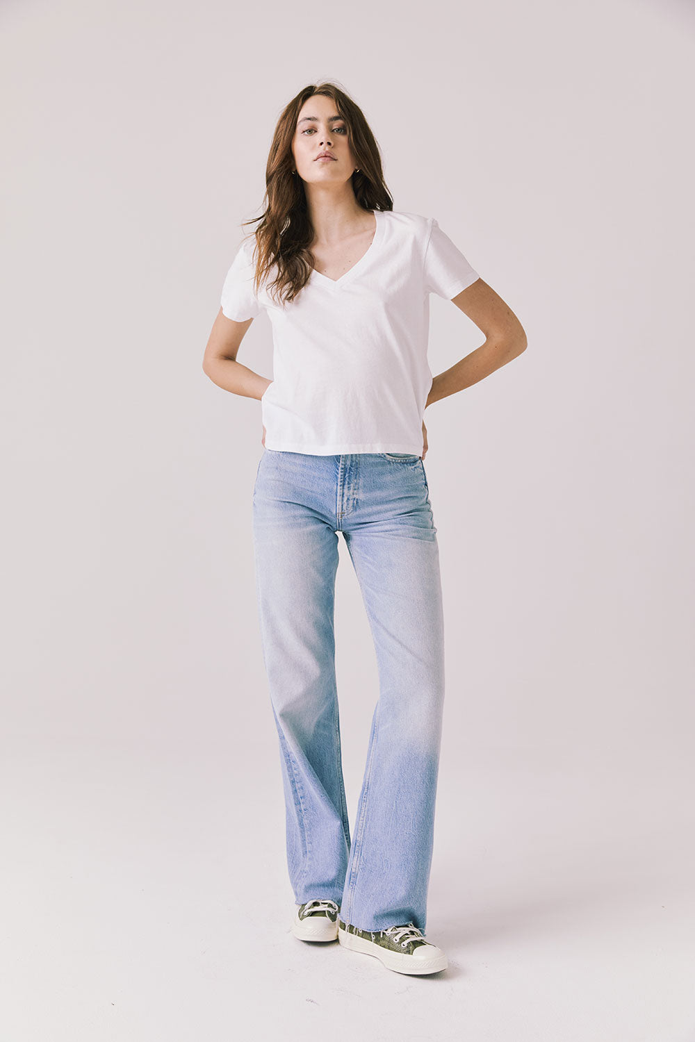 Full body view of woman wearing Chaser’s Gimlet White Tee with blue jeans on a plain background