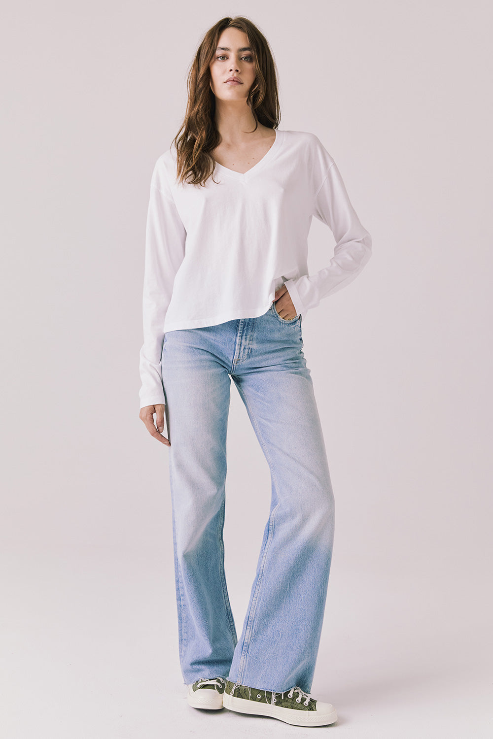 Full body view of woman wearing Chaser’s Whiskey White Long Sleeve paired with blue jeans on a plain background