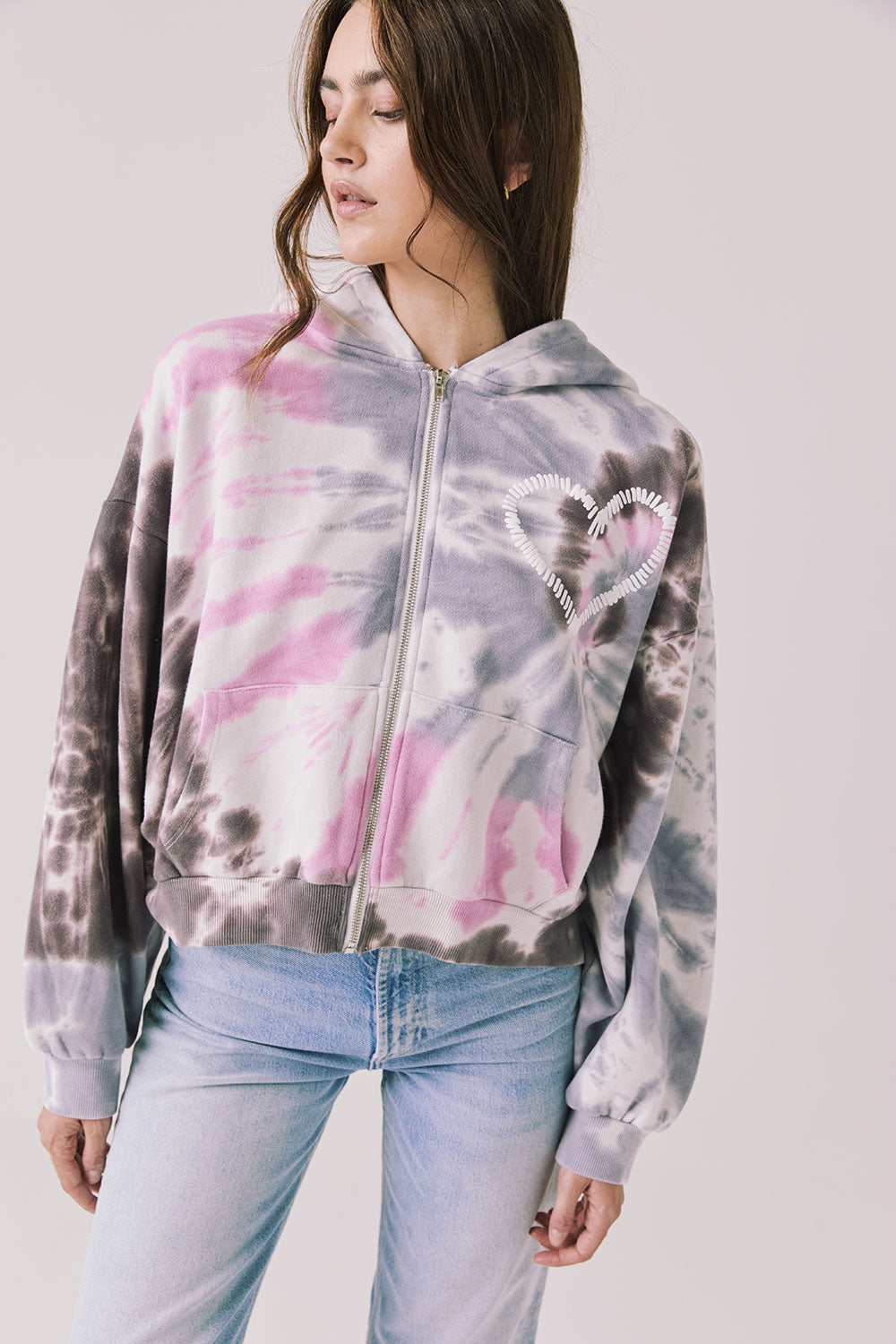 Front view of woman wearing Chaser’s Heart Tie Dye Zip Up Hoodie with heart embroidery on the left chest on a white background