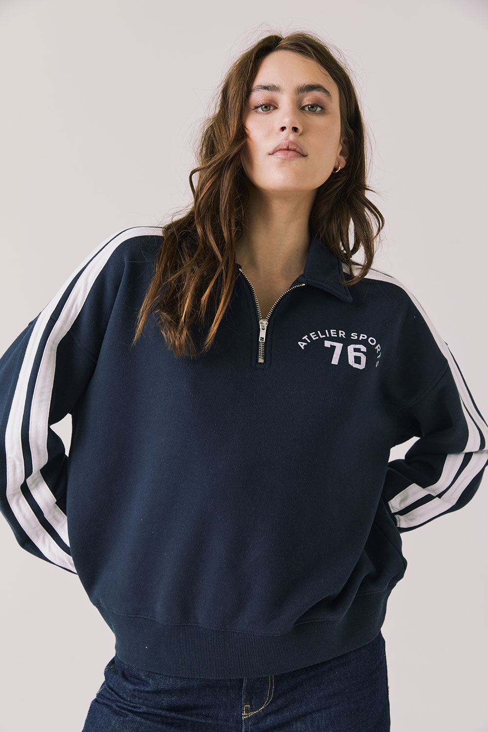 Woman wearing Chaser's navy Atelier Sports 76 Half Zip Long Sleeve with white stripes on a light gray background
