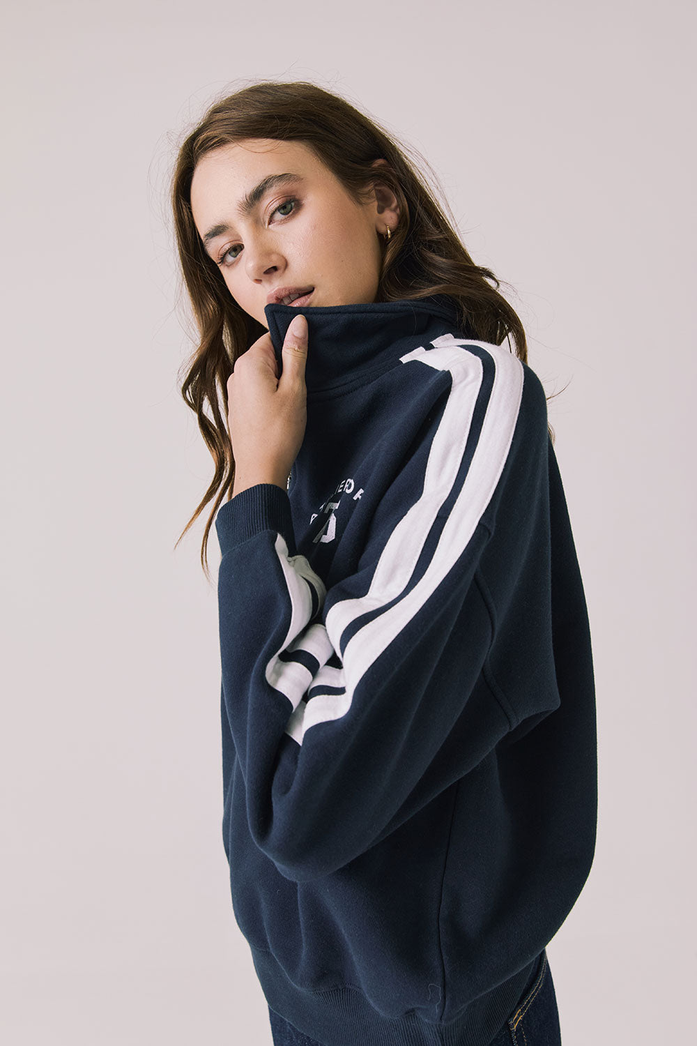 Side view of woman wearing Chaser's navy Atelier Sports 76 Half Zip Long Sleeve with white stripes on a light gray background