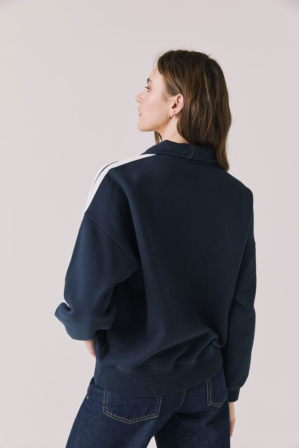 Back view of woman wearing Chaser's navy Atelier Sports 76 Half Zip Long Sleeve with white stripes on a light gray background