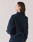 Back view of woman wearing Chaser's navy Atelier Sports 76 Half Zip Long Sleeve with white stripes on a light gray background
