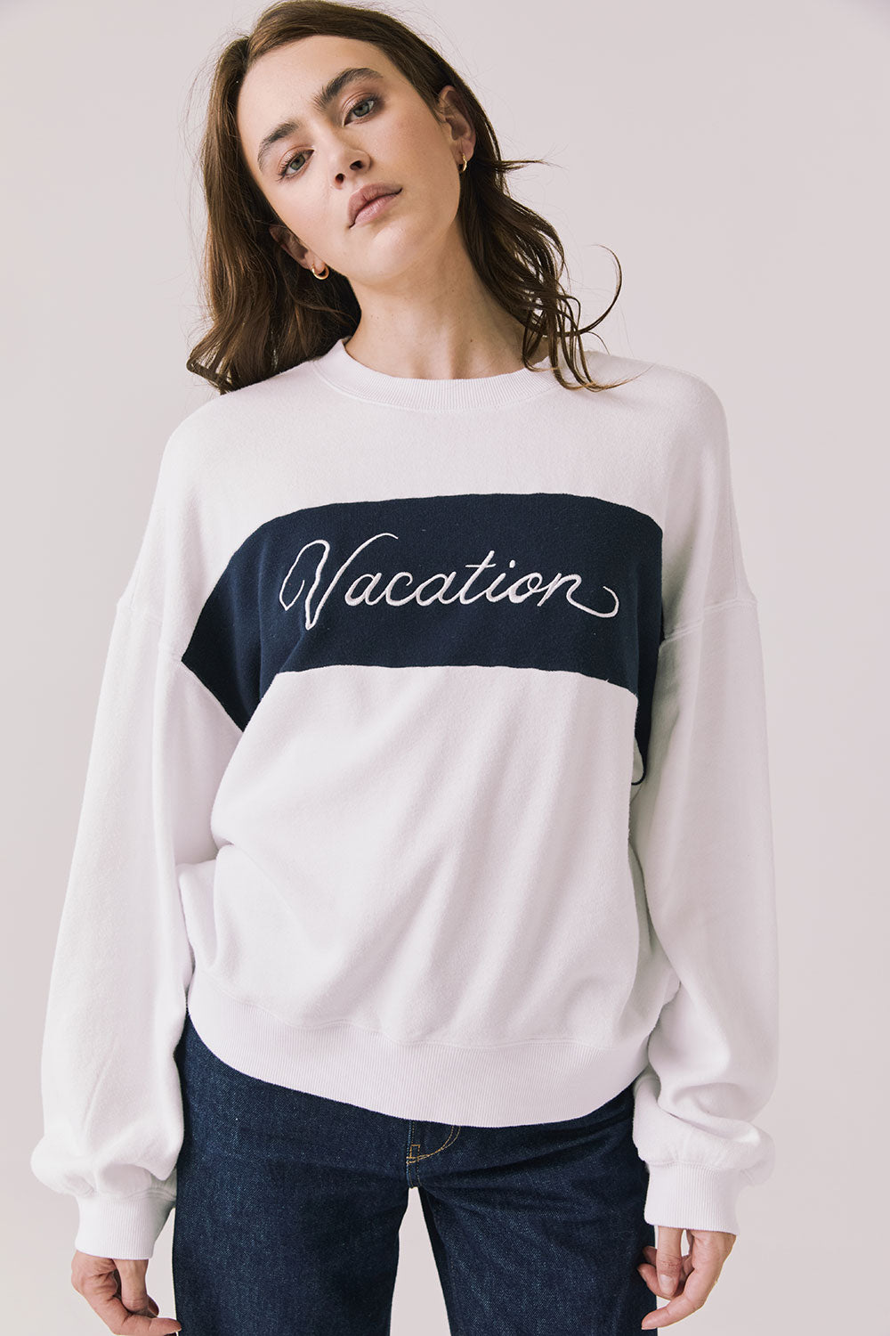 Front view of woman wearing Chaser’s white Vacation Long Sleeve with red ‘Vacation’ text on a light background