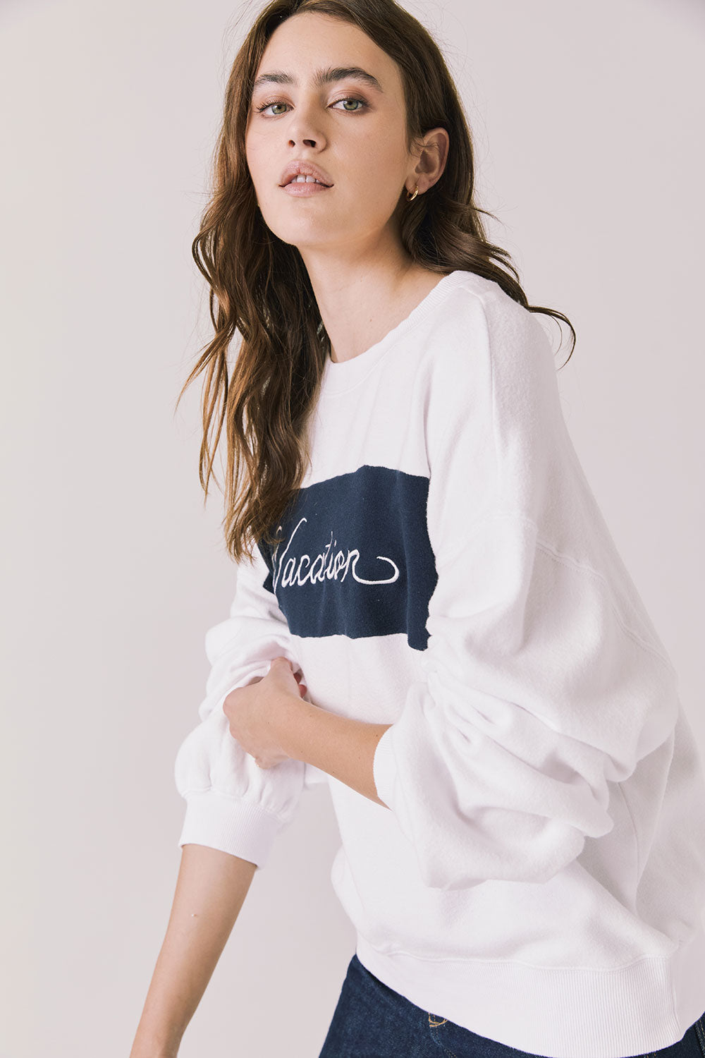 Side view of woman wearing Chaser’s white Vacation Long Sleeve with ‘Vacation’ graphic on a light background