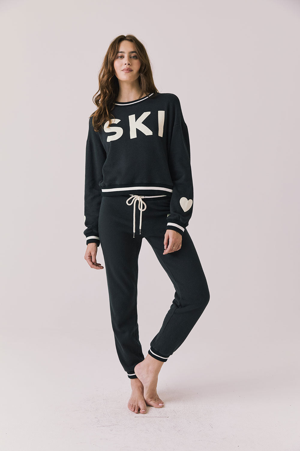Full body view of woman wearing Chaser’s Ski True Black Long Sleeve Pullover with matching Heart Joggers on a white background