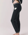 Side view of woman wearing Chaser’s Heart True Black Joggers with heart design and white tie on a white background