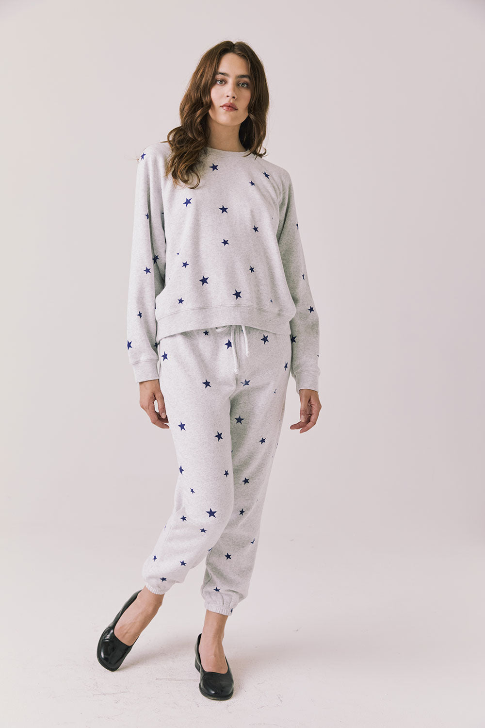 Full body view of woman wearing Chaser’s Festive Stars Pullover in Light Grey with star patterns and matching Festive Stars Joggers on a white background