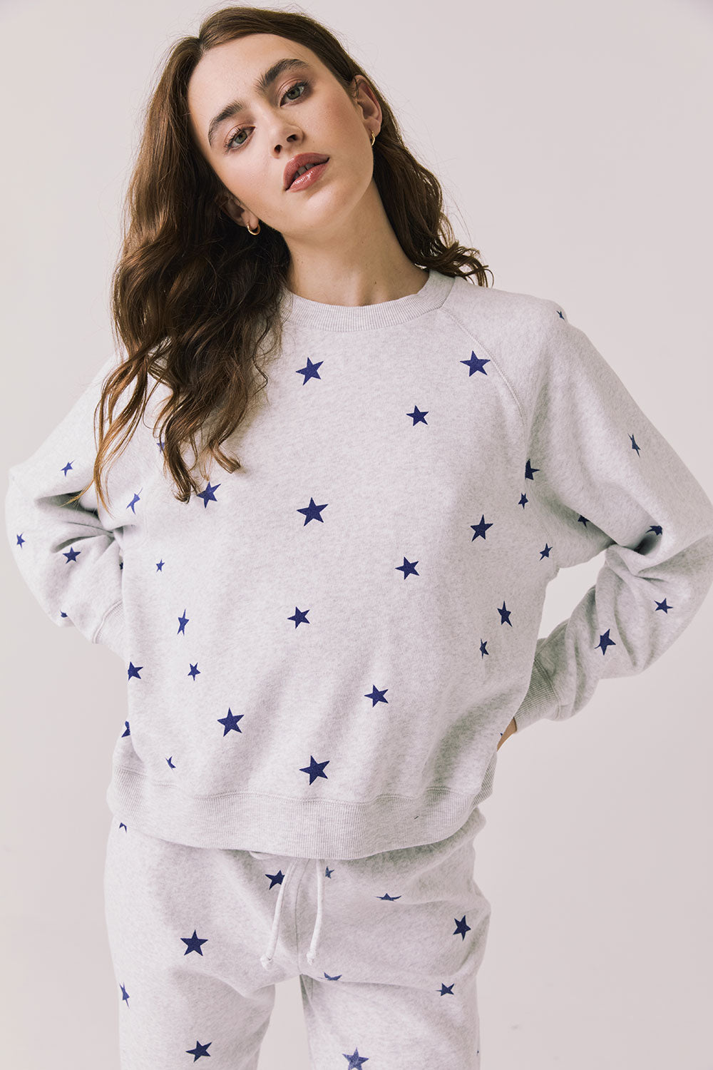 Front view of woman wearing Chaser’s Festive Stars Pullover in Light Grey with star patterns on a white background