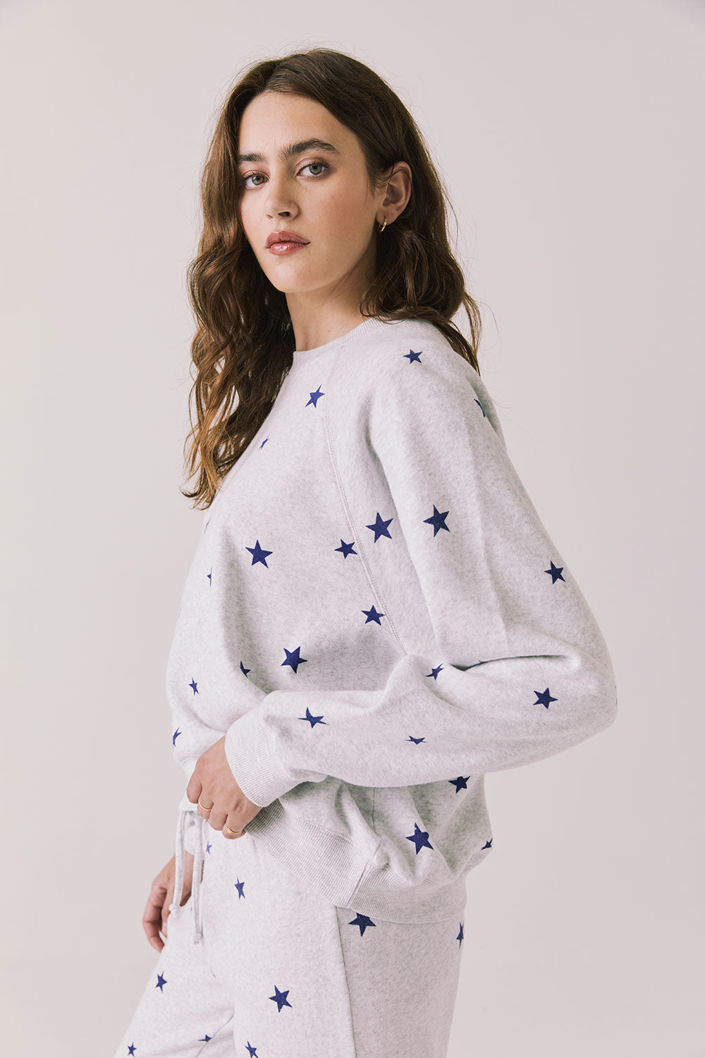 Side view of woman wearing Chaser’s Festive Stars Pullover in Light Grey with star patterns on a white background