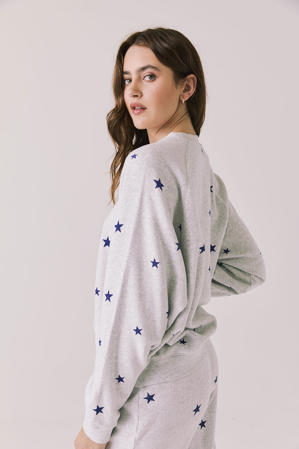 Back view of woman wearing Chaser’s Festive Stars Pullover in Light Grey with star patterns on a white background