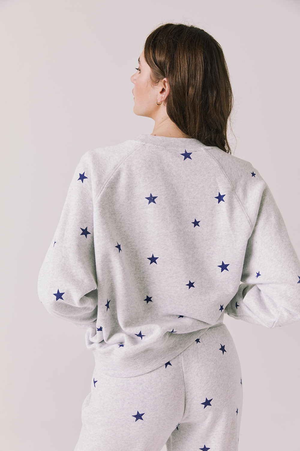 Back view of woman wearing Chaser’s Festive Stars Pullover in Light Grey with star patterns on a white background