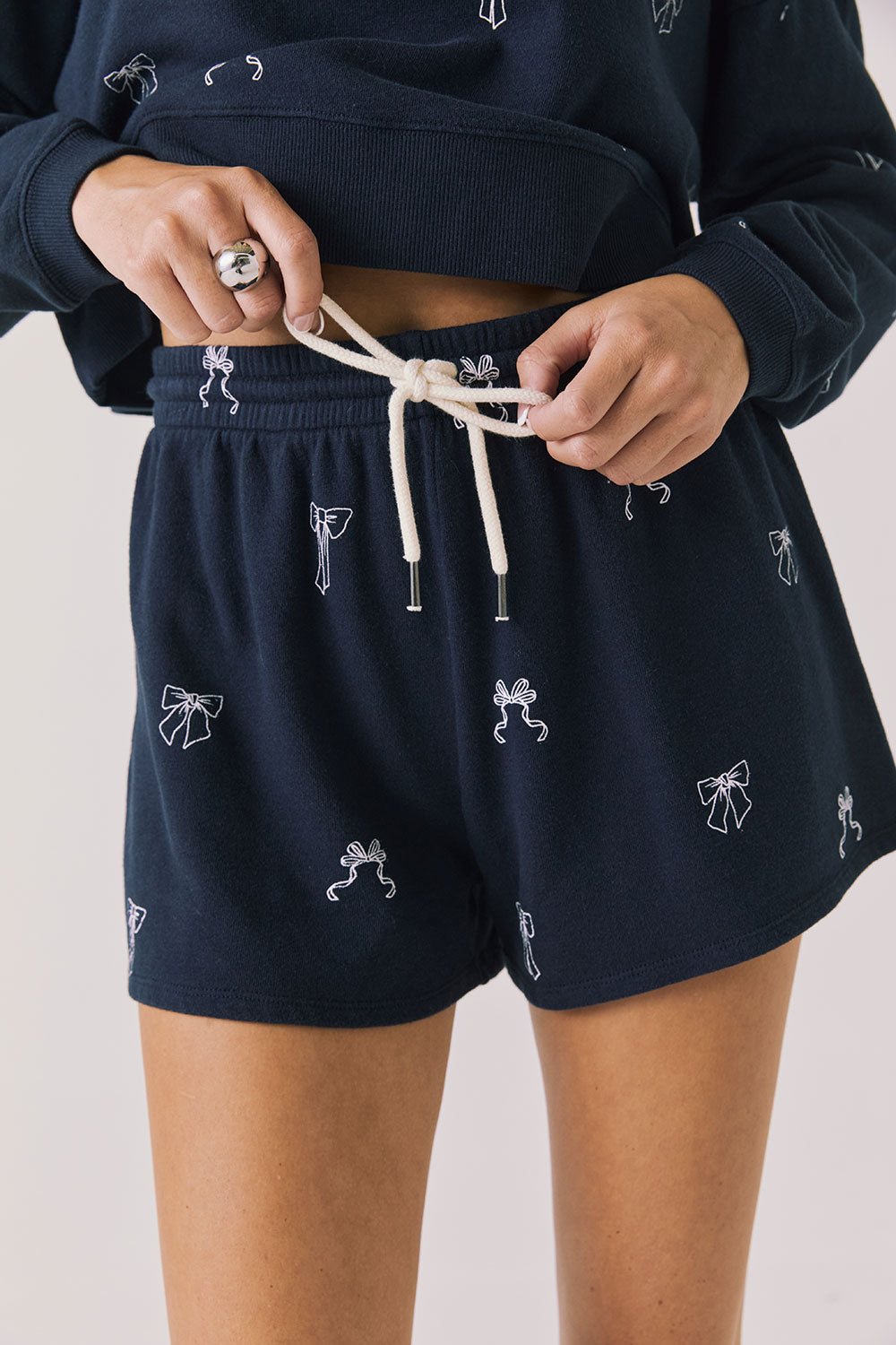 Front view of woman wearing Chaser’s navy Tossed Bows Shorts with small bow prints on a white background