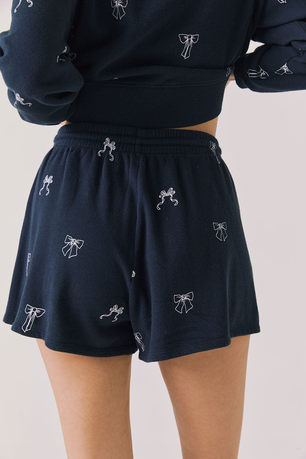 Back view of woman wearing Chaser’s navy Tossed Bows Shorts with allover bow pattern on a white background