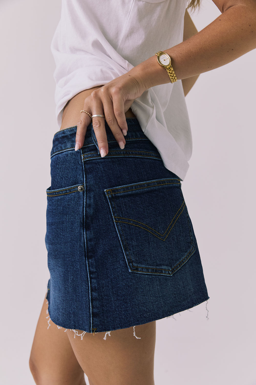 Angled side-back view of the Chaser Sloane Mini Skirt in Indigo Wash showing pocket stitching and raw hem detail