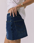 Angled side-back view of the Chaser Sloane Mini Skirt in Indigo Wash showing pocket stitching and raw hem detail