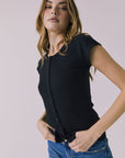 3/4 view of a woman wearing the Chaser Anchor Black Tee with buttons and blue jeans against a plain background