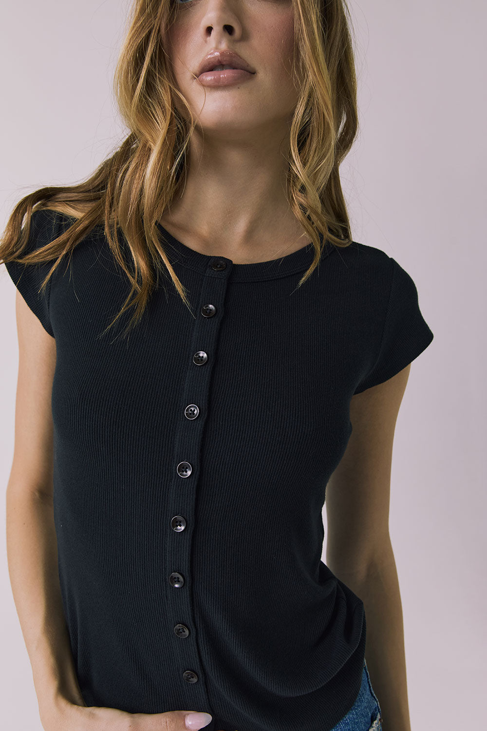 Close up view of a woman wearing the Chaser Anchor Black Tee with buttons and blue jeans against a plain background