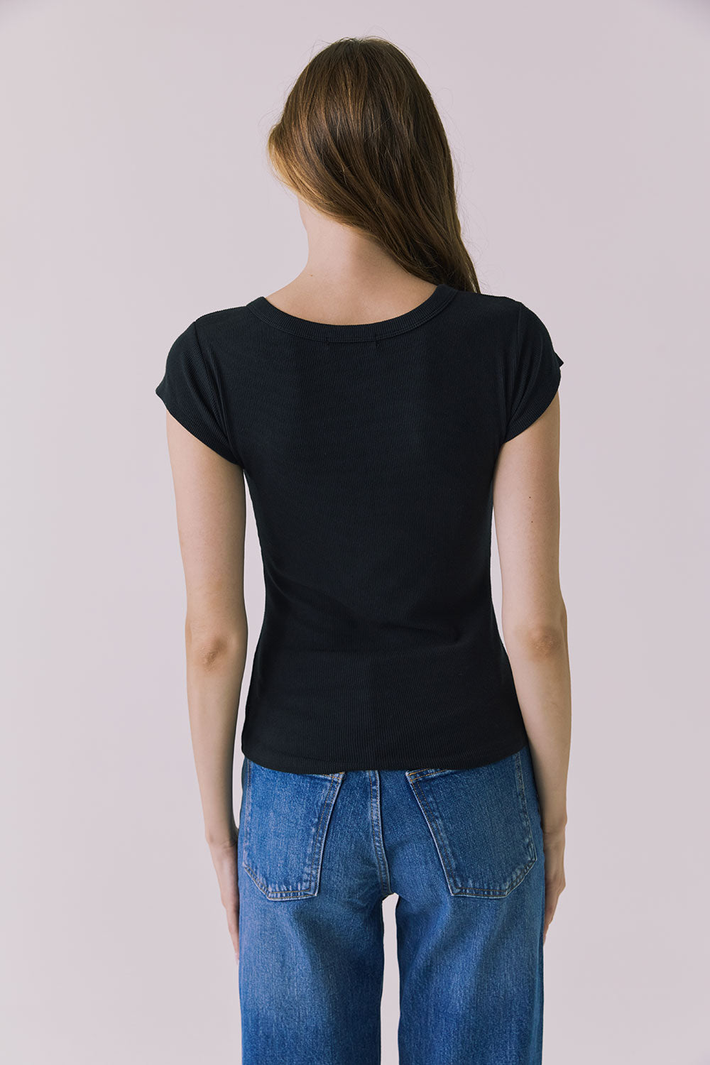 Back view of a woman wearing the Chaser Anchor Black Tee with buttons and blue jeans against a plain background