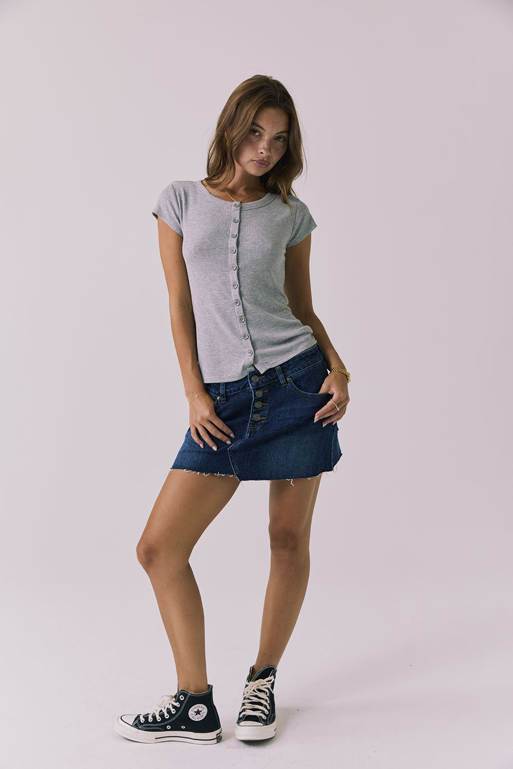 Full body view of a woman wearing Chaser's heather gray button-up Anchor Tee and the Sloane Mini Skirt against a plain background
