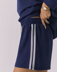 Side view of a woman wearing Chaser's navy blue Cornell Sapphire & Heather Grey Hanoverr shorts on a plain background
