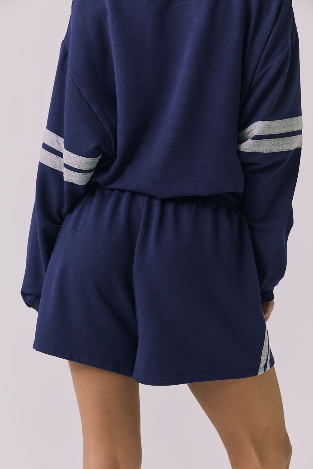 Back view of a woman wearing Chaser's navy blue Cornell Sapphire & Heather Grey Hanoverr shorts on a plain background