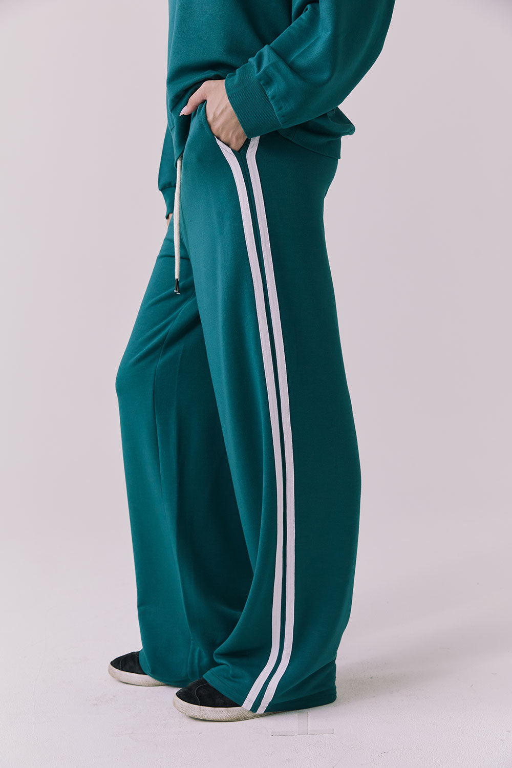 Saltwater Luxe Sandi Joggers in Teal with White side stripes shown from the side emphasizing the straight leg silhouette and sporty contrast trim with the matching Cornell Pullover partially visible