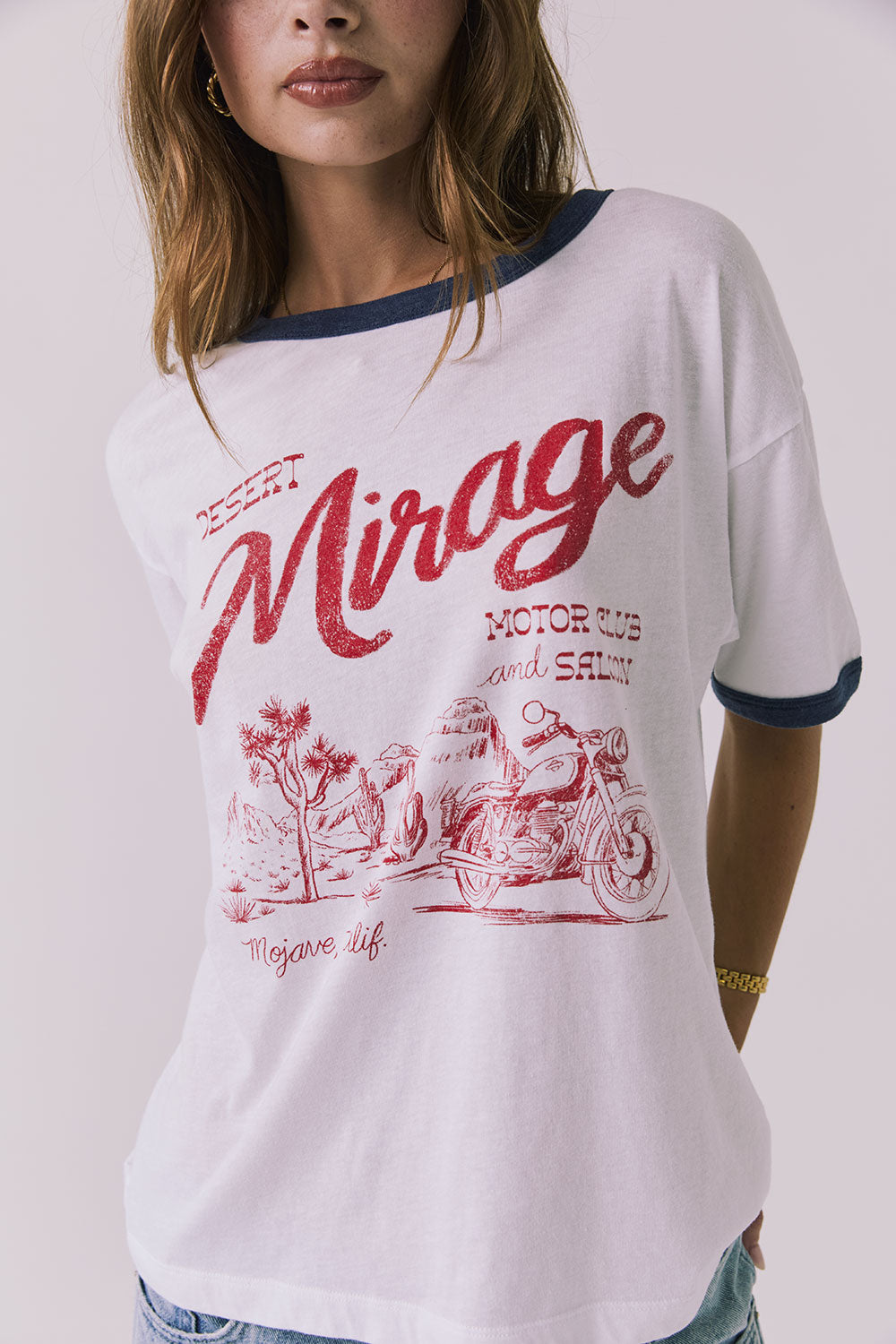 Close up of a woman wearing Chaser's white Desert Mirage Motor Club Tee with red text and graphics on a plain background