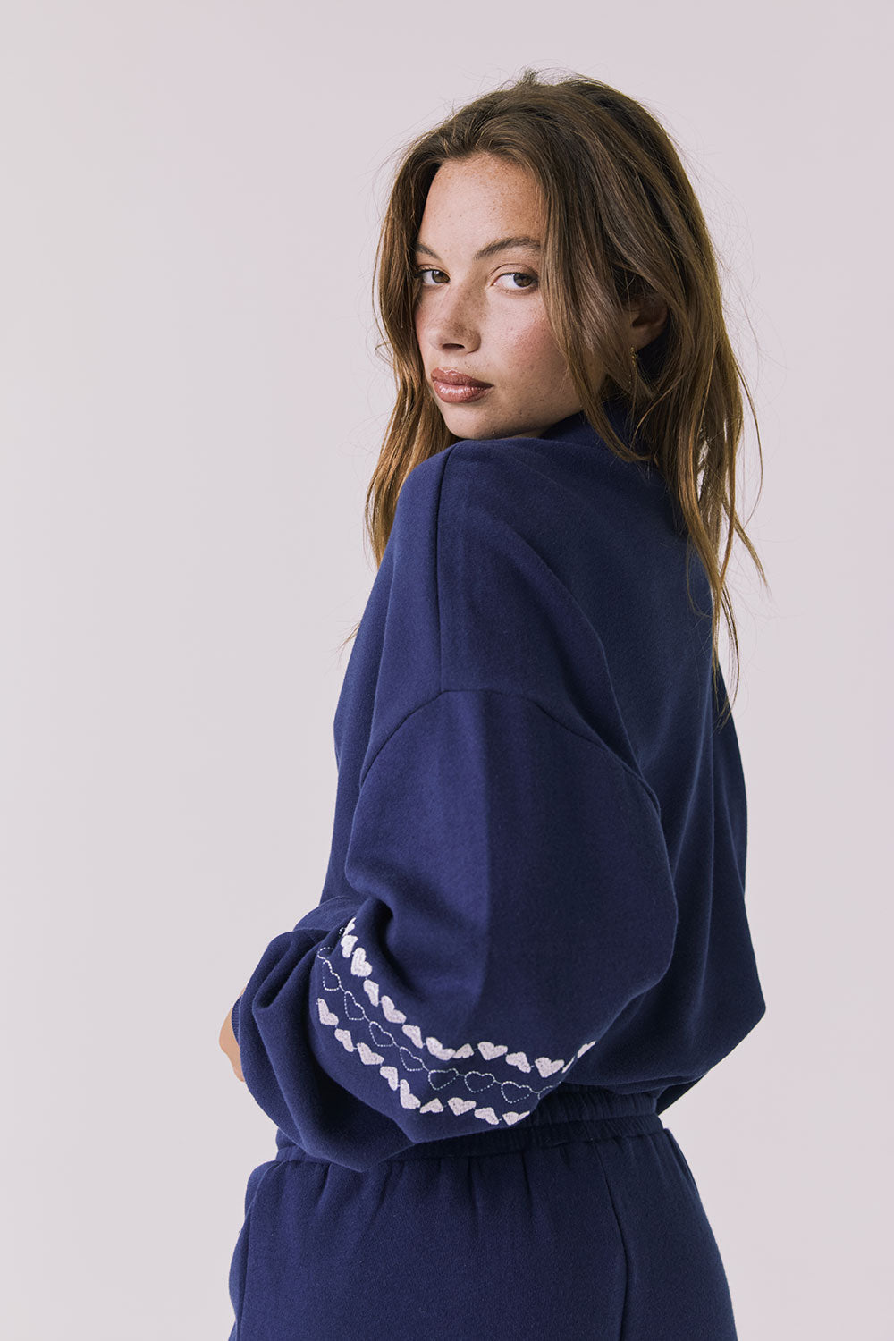 Back view of woman wearing Chaser's navy blue Heart Stitches Pullover Hoodie on a plain background