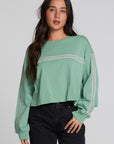 A woman modeling a sage green cropped sweatshirt with light gray stripe details on the chest and sleeves, paired with black jeans, against a solid light gray background