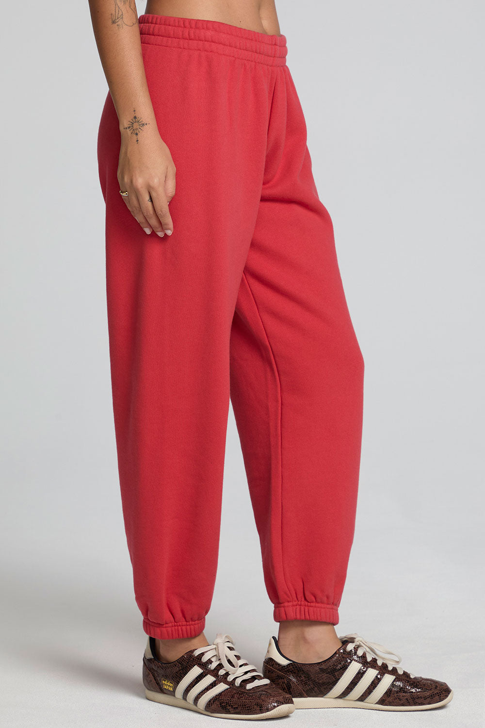 Side view of a woman wearing the Chaser Ada Dry Red Jogger on a neutral background with arms at sides and sneakers 