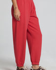 Side view of a woman wearing the Chaser Ada Dry Red Jogger on a neutral background with arms at sides and sneakers 